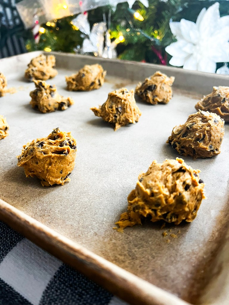 Raw pumpkin chocolate chip cookie dough on a baking sheet with festive holiday decorations in the background.