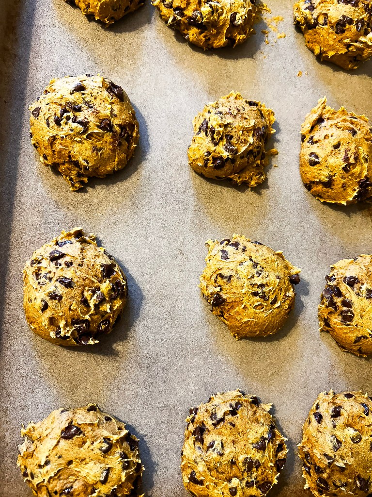 Scoops of pumpkin chocolate chip cookie dough arranged on parchment paper, ready for baking.
