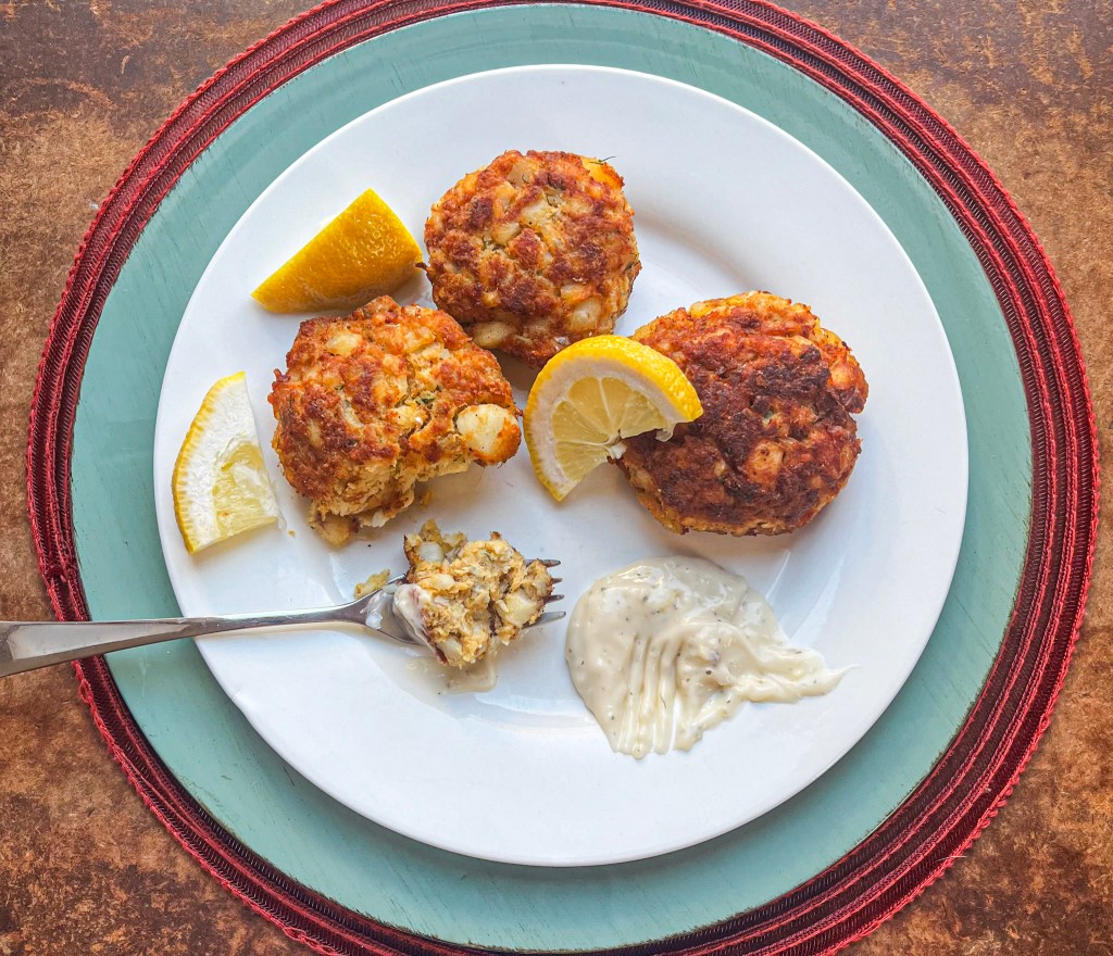 Three golden-brown cod cakes on a white plate with lemon wedges and tartar sauce, ready to be enjoyed.
